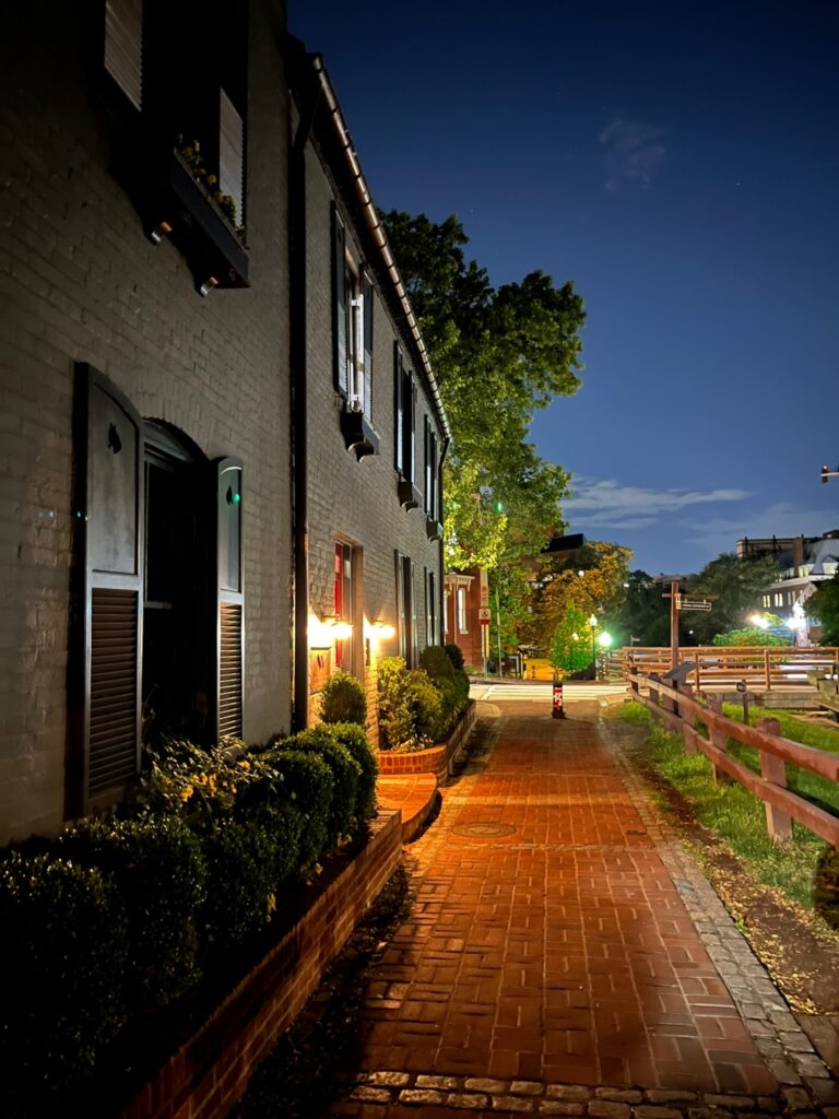 Quiet cobblestone alley in Georgetown lit by warm lamps at night.