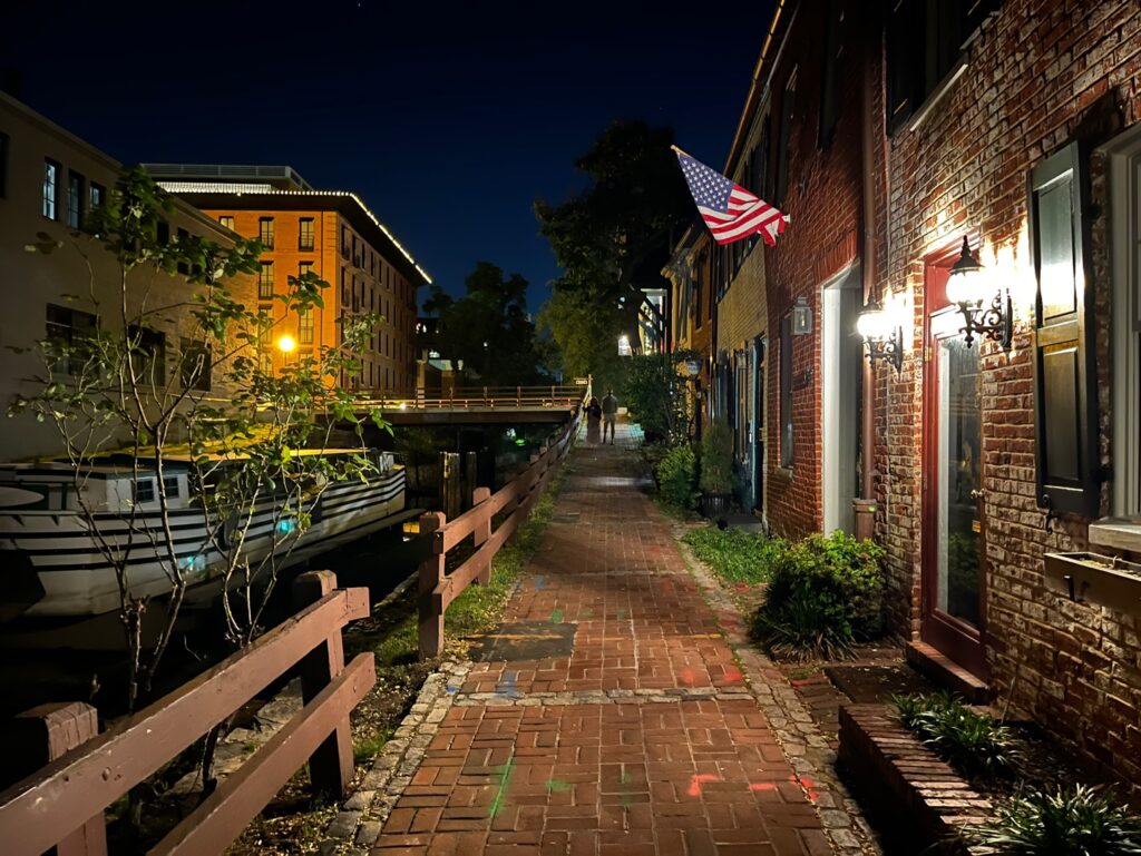 C&O Canal-side brick pathway at night with American flags and reflections.